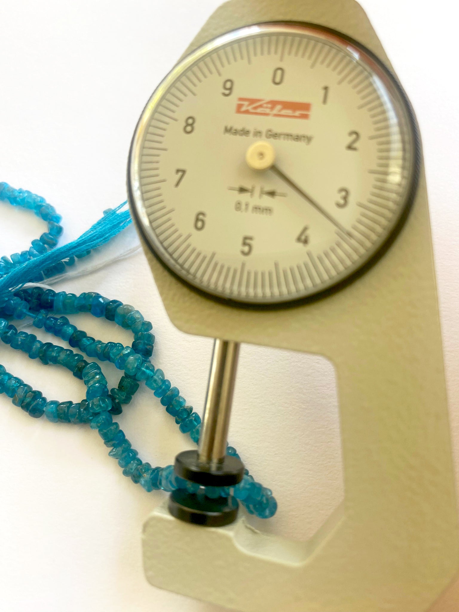 A dial gauge measures the neon apatite smooth wheel 4.0–4.2mm gemstone.