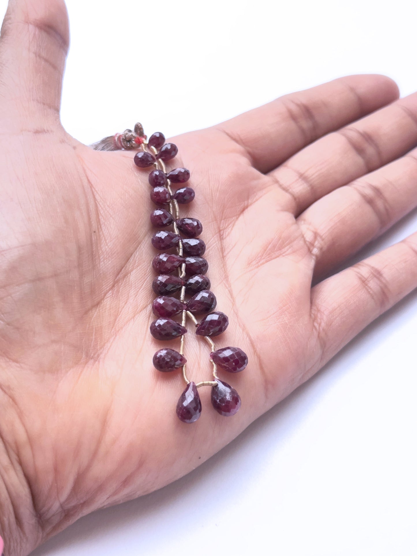 A person holds delicate strands of ruby beads, showcasing their smooth design.