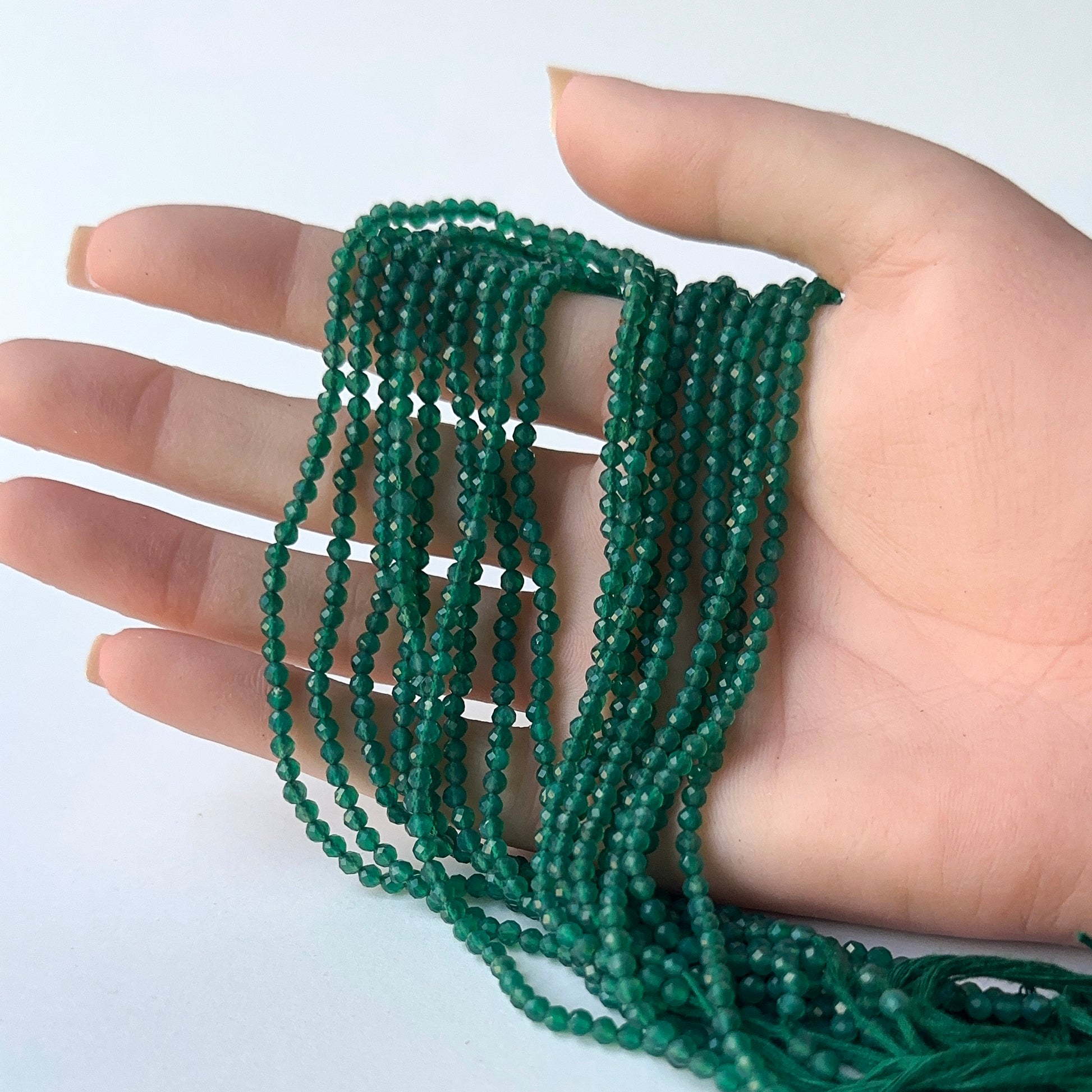 A person holds delicate strands of Onyx beads, showcasing their faceted rondelle design.