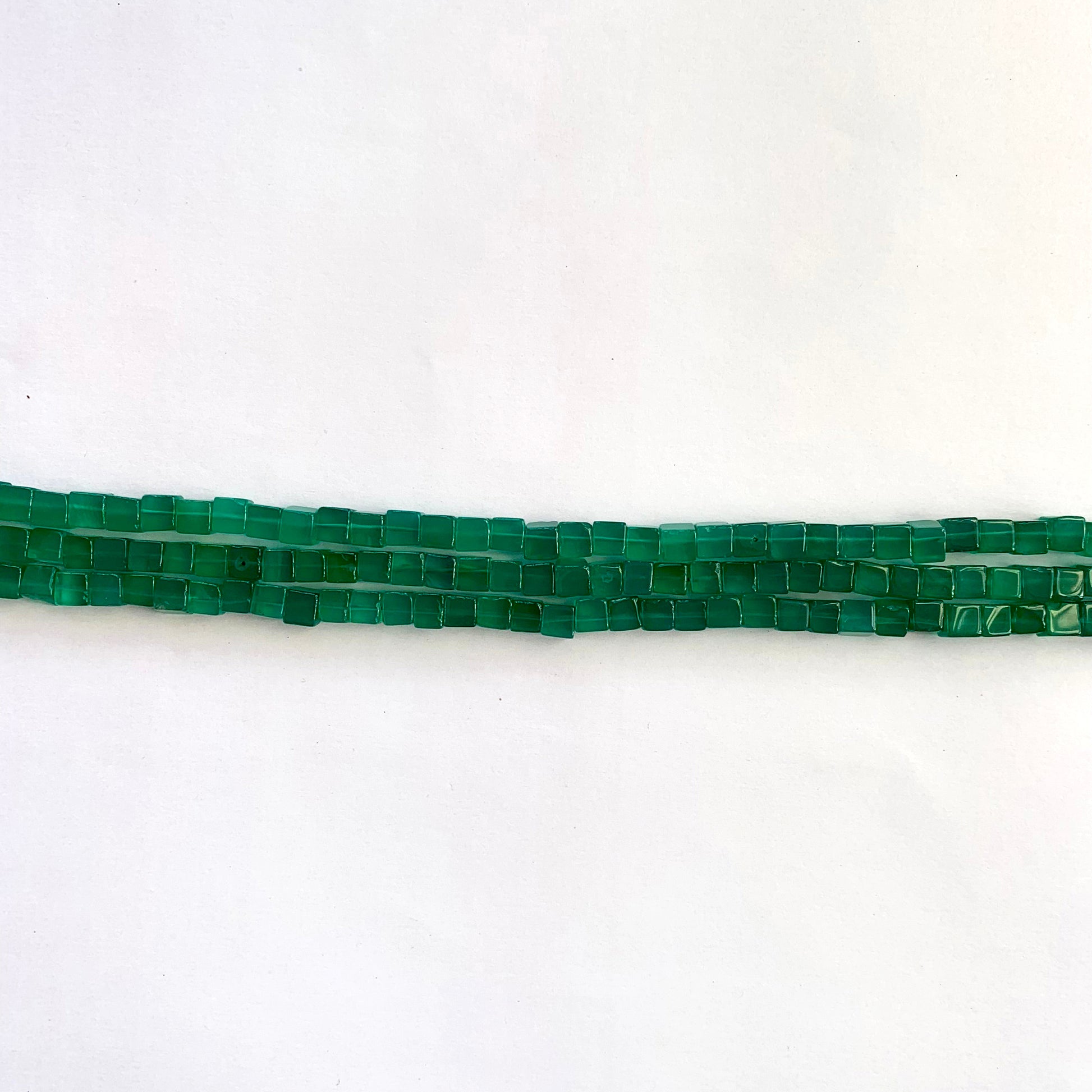 Detailed view of green Onyx cube beads with sharp edges and a radiant shine on each facet. 