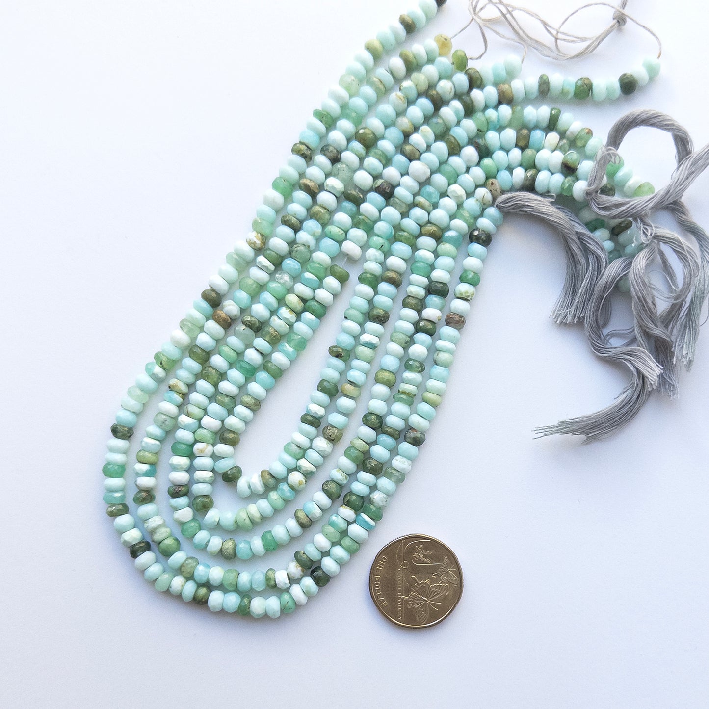 A coin is placed near delicate strands of Mint Green Opal beads for scale.