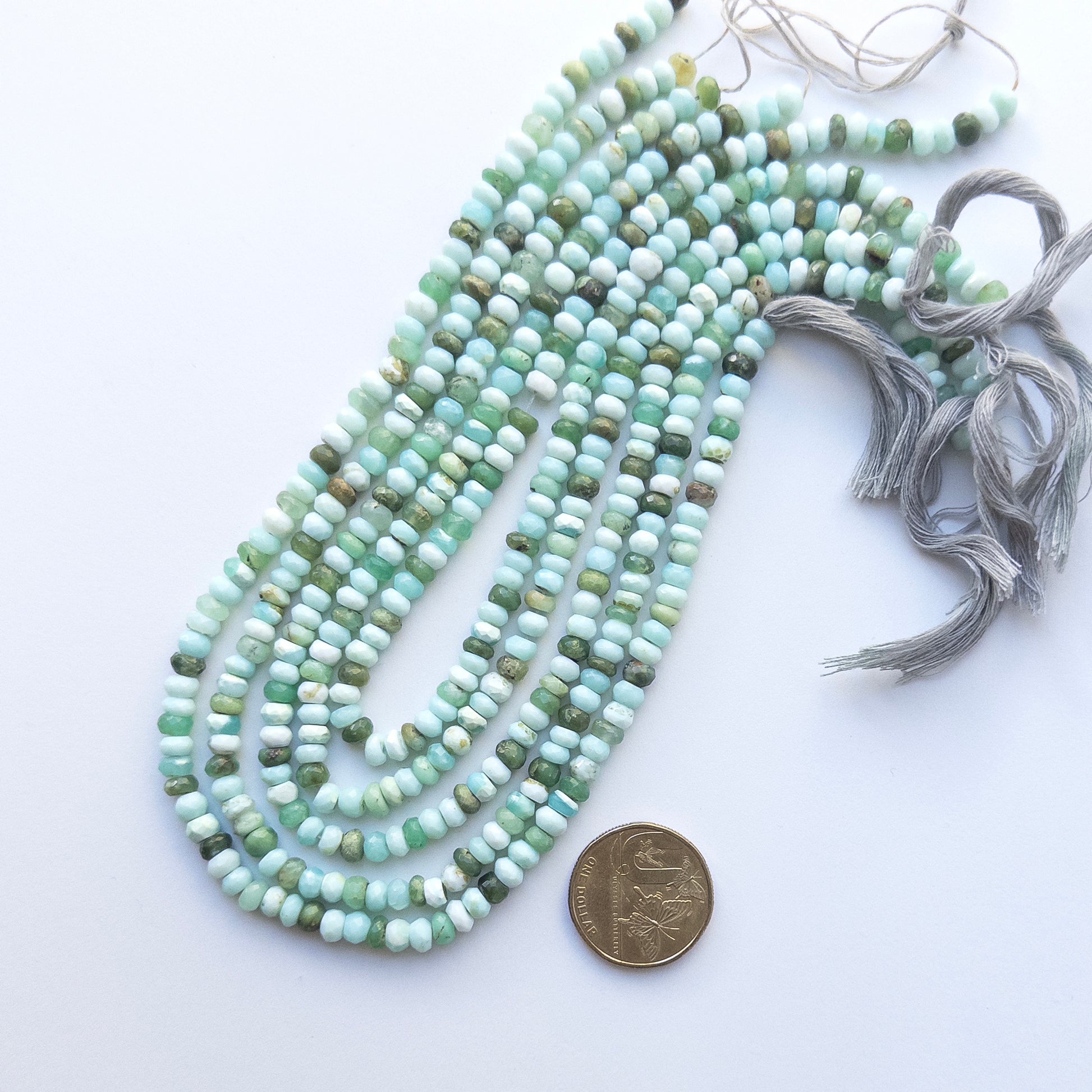 A coin is placed near delicate strands of Mint Green Opal beads for scale.
