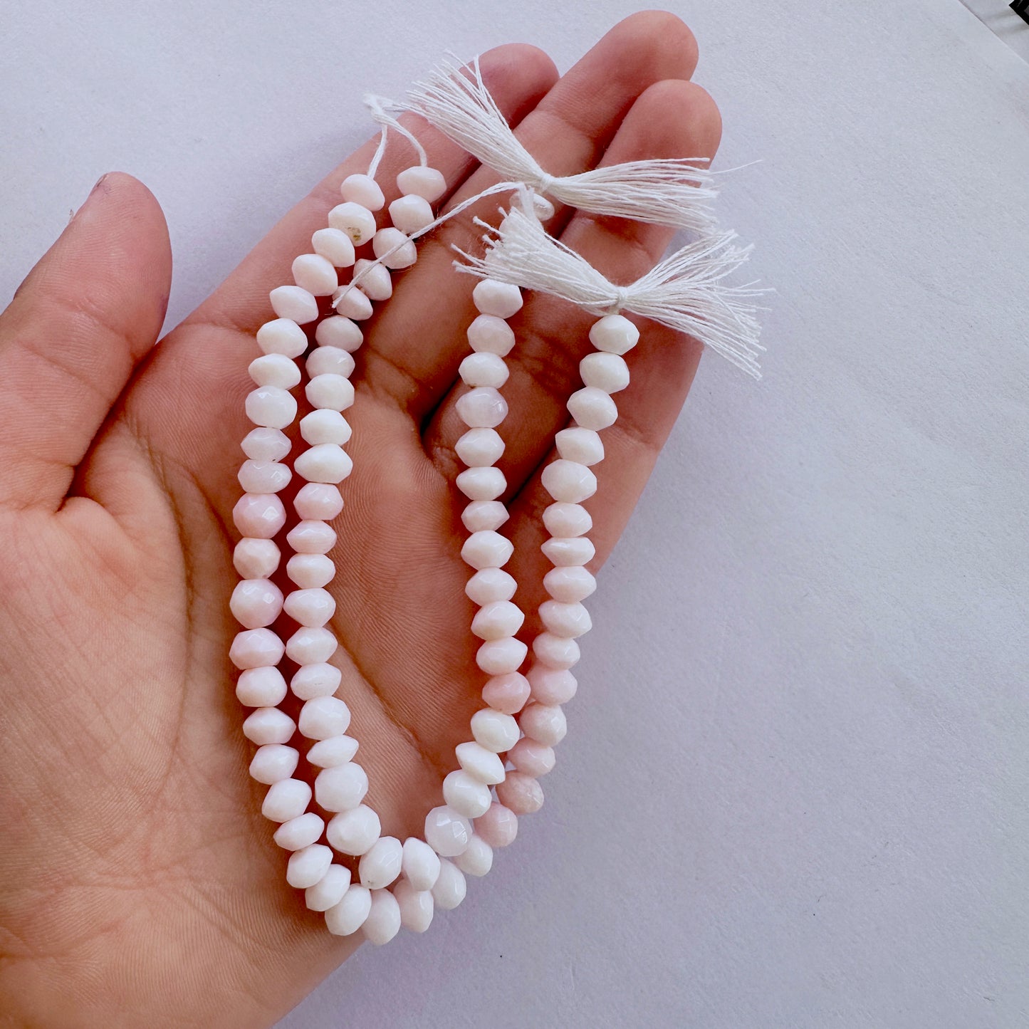 A person holds delicate strands of Opal beads, showcasing their faceted design.