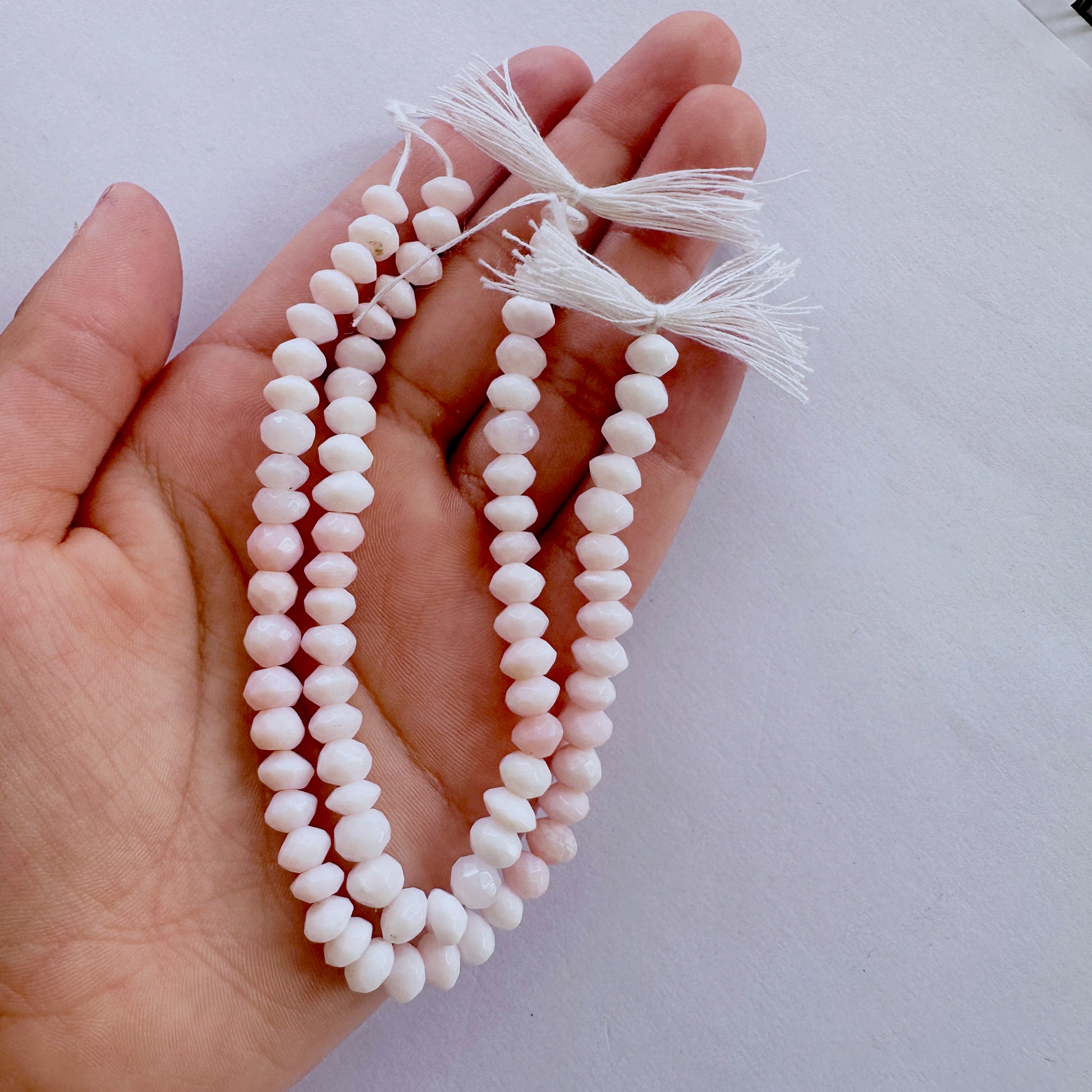 A person holds delicate strands of Opal beads, showcasing their faceted design.