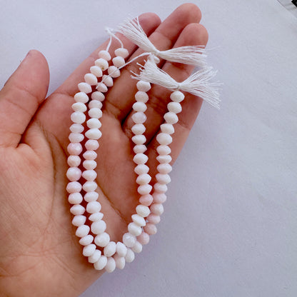 A person holds delicate strands of Opal beads, showcasing their faceted design.
