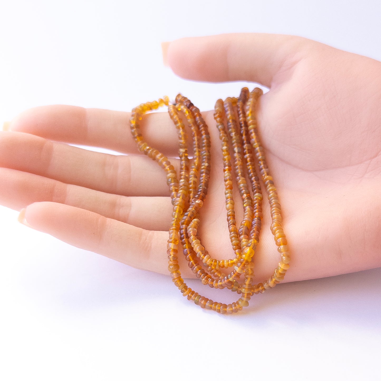 A person holds delicate strands of Opal beads, showcasing their smooth rondelle design.