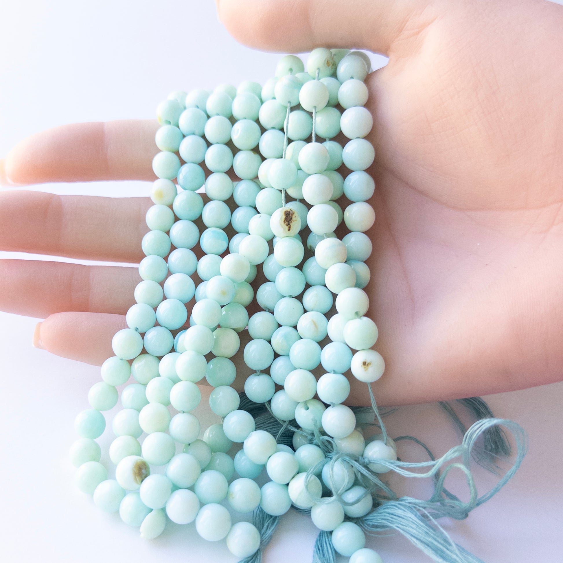 A person holds delicate strands of Opal beads, showcasing their smooth round design.