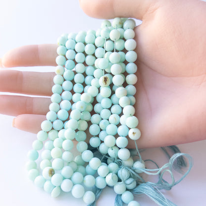 A person holds delicate strands of Opal beads, showcasing their smooth round design.