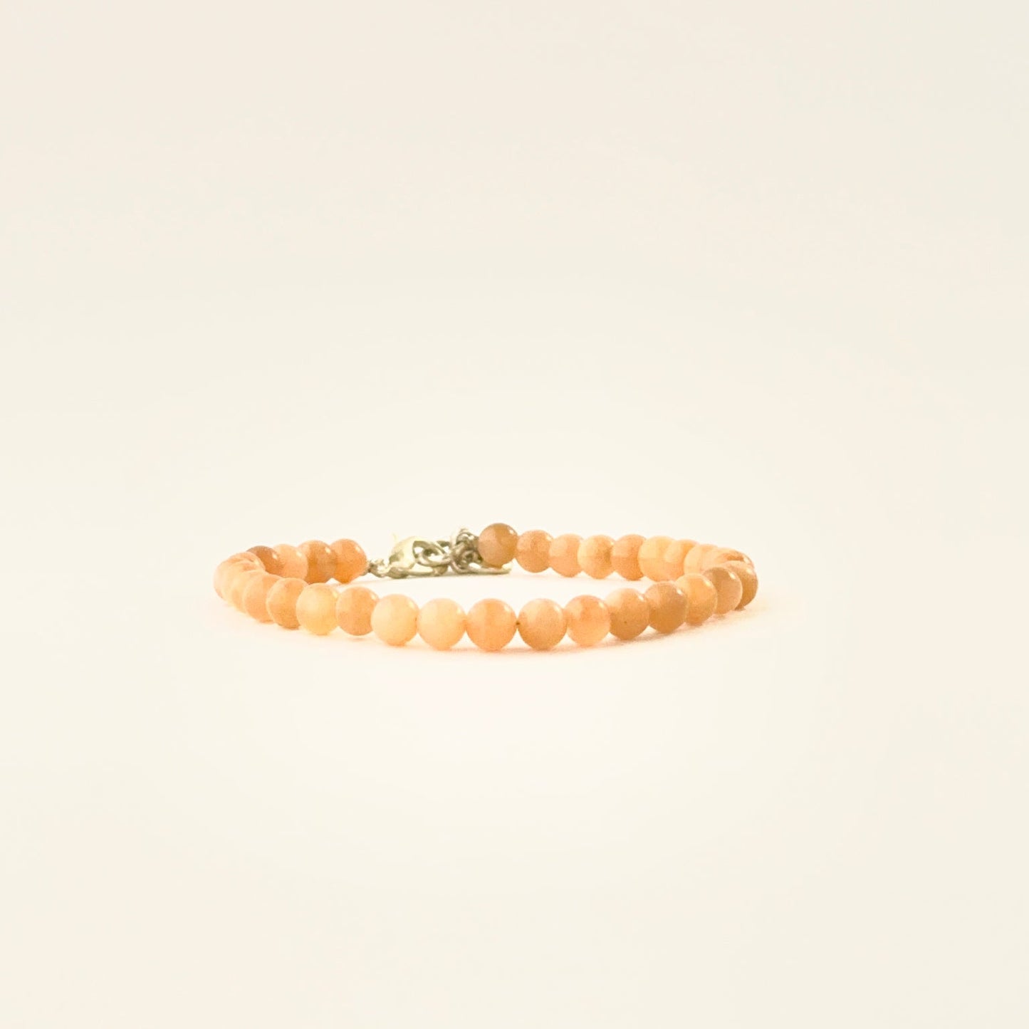 Smooth round peach moonstone bead bracelet arranged in a single adjustable strand.