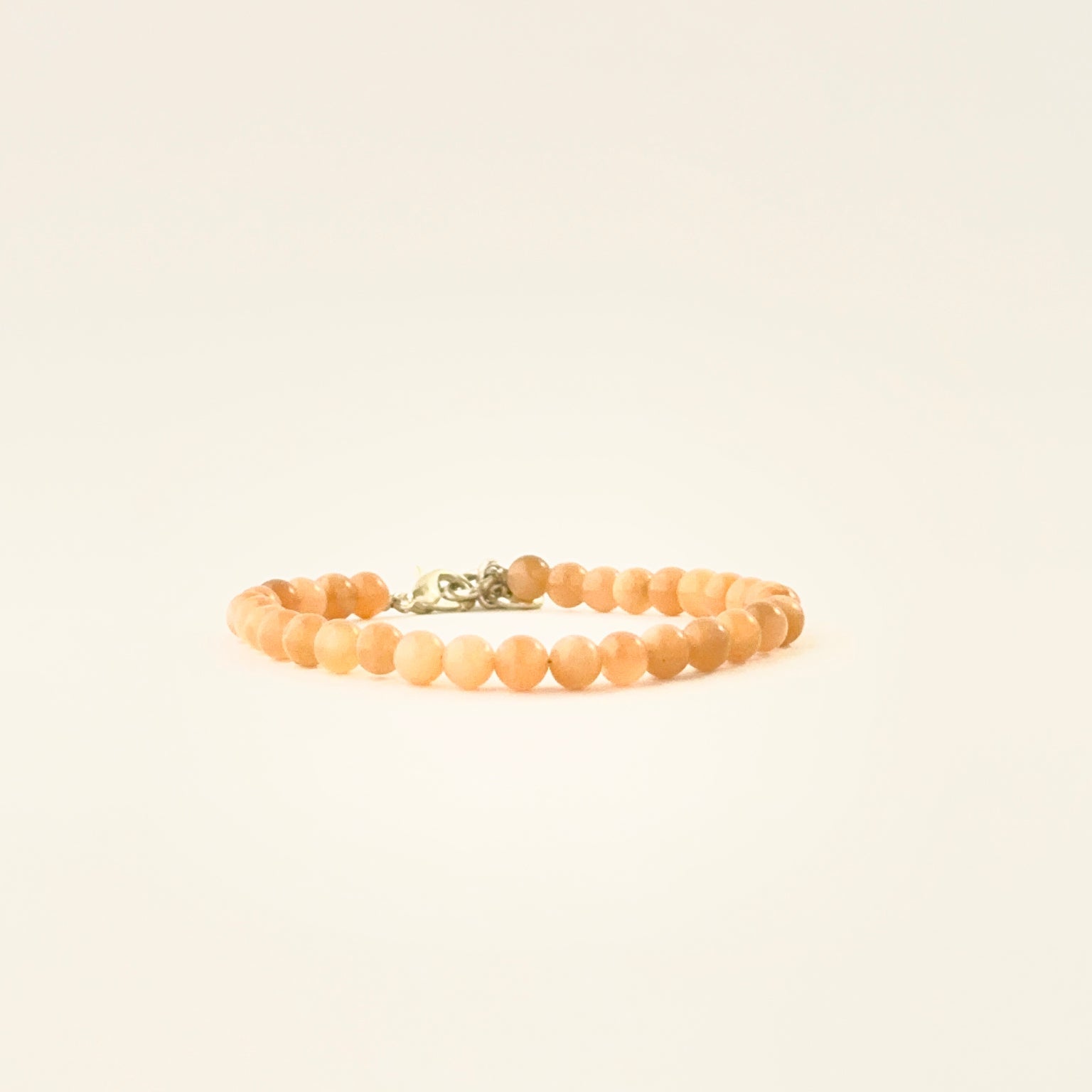 Smooth round peach moonstone bead bracelet arranged in a single adjustable strand.