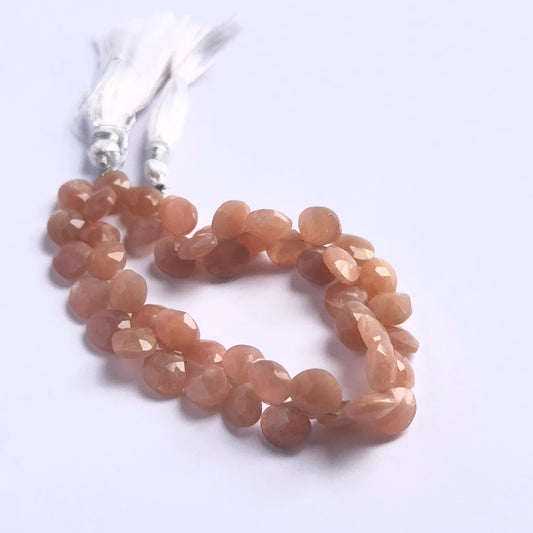 Close-up of natural gemstone beads showing the faceted briolette cut and warm peach moonstone glow.