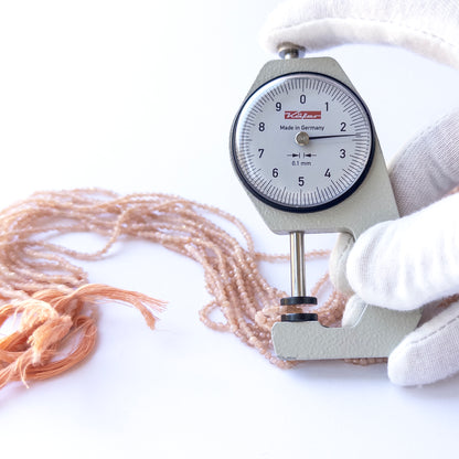 A dial gauge measures the Peach Moonstone faceted rondelle 2.4mm gemstone.
