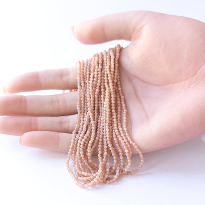 A person holds delicate strands of Peach Moonstone beads, showcasing their faceted rondelle design.