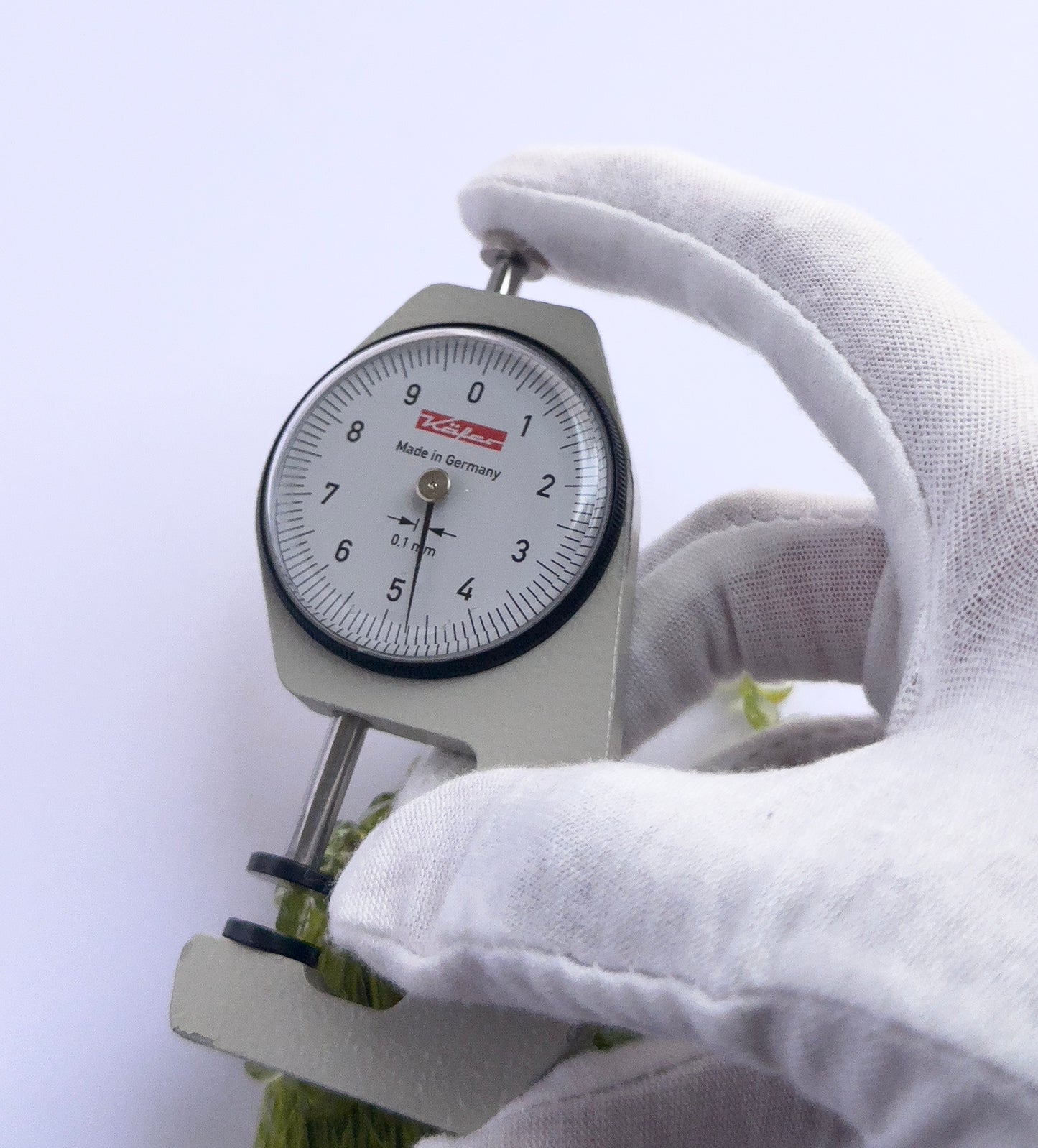 A dial gauge measures the Peridot smooth drop 4–5mm gemstone.
