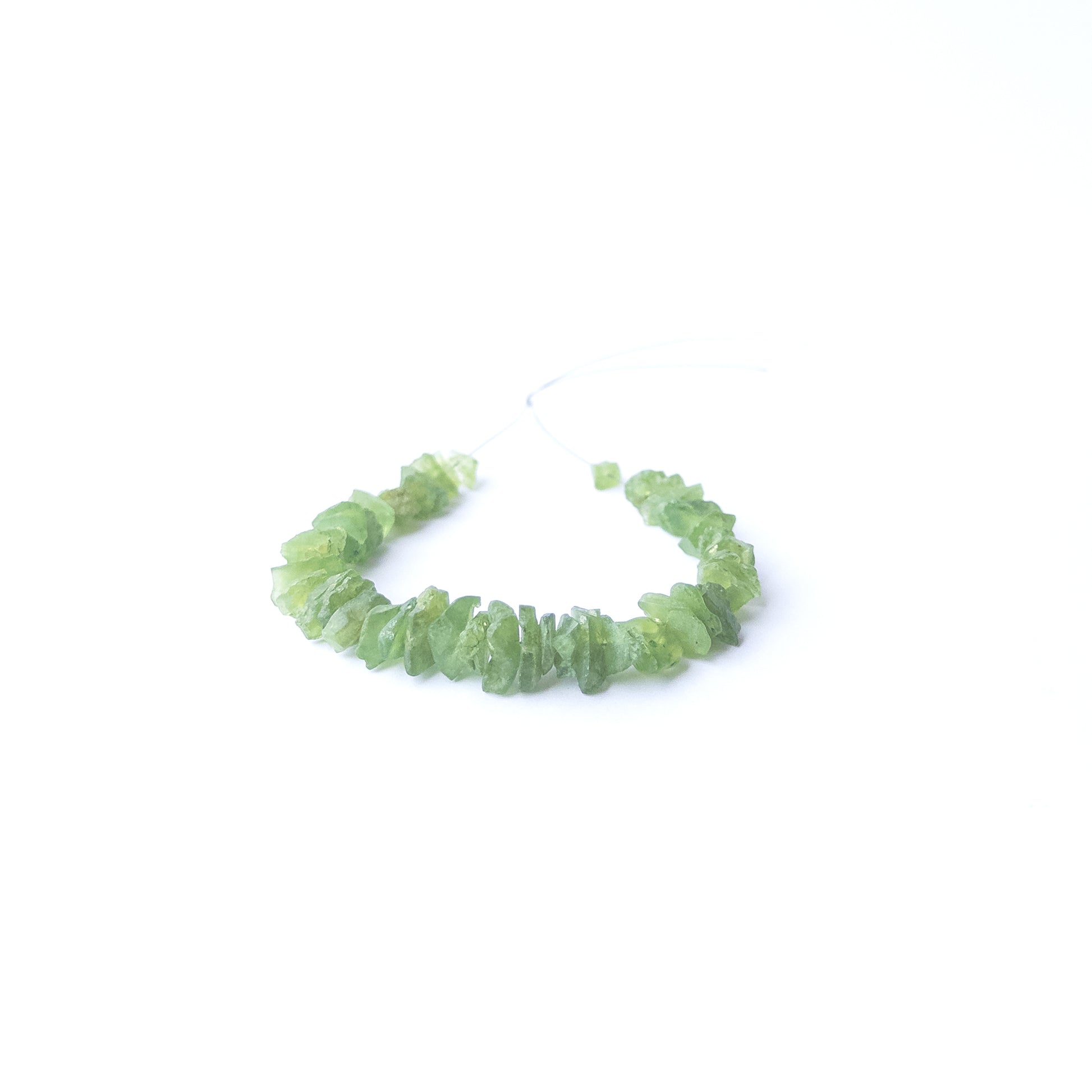 Premium Peridot drilled rough beads arranged neatly to display their fresh green hue and raw beauty.