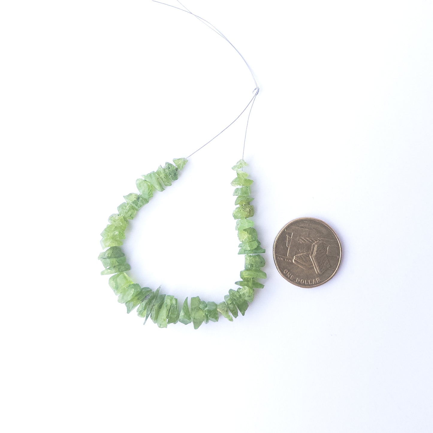 A coin is place near delicate pieces of Peridot beads for scale.