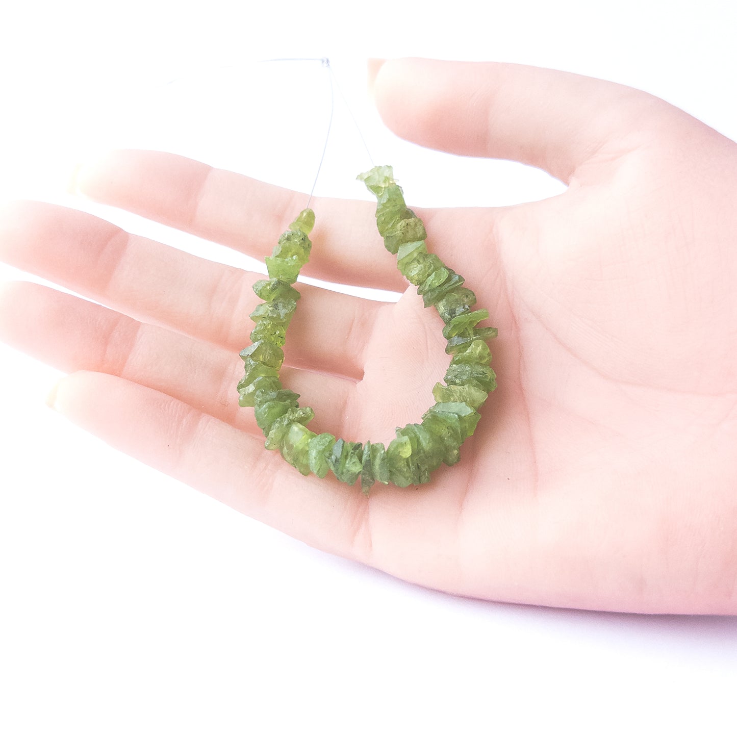 A person holds delicate strands of Peridot beads, showcasing their drilled rough design.