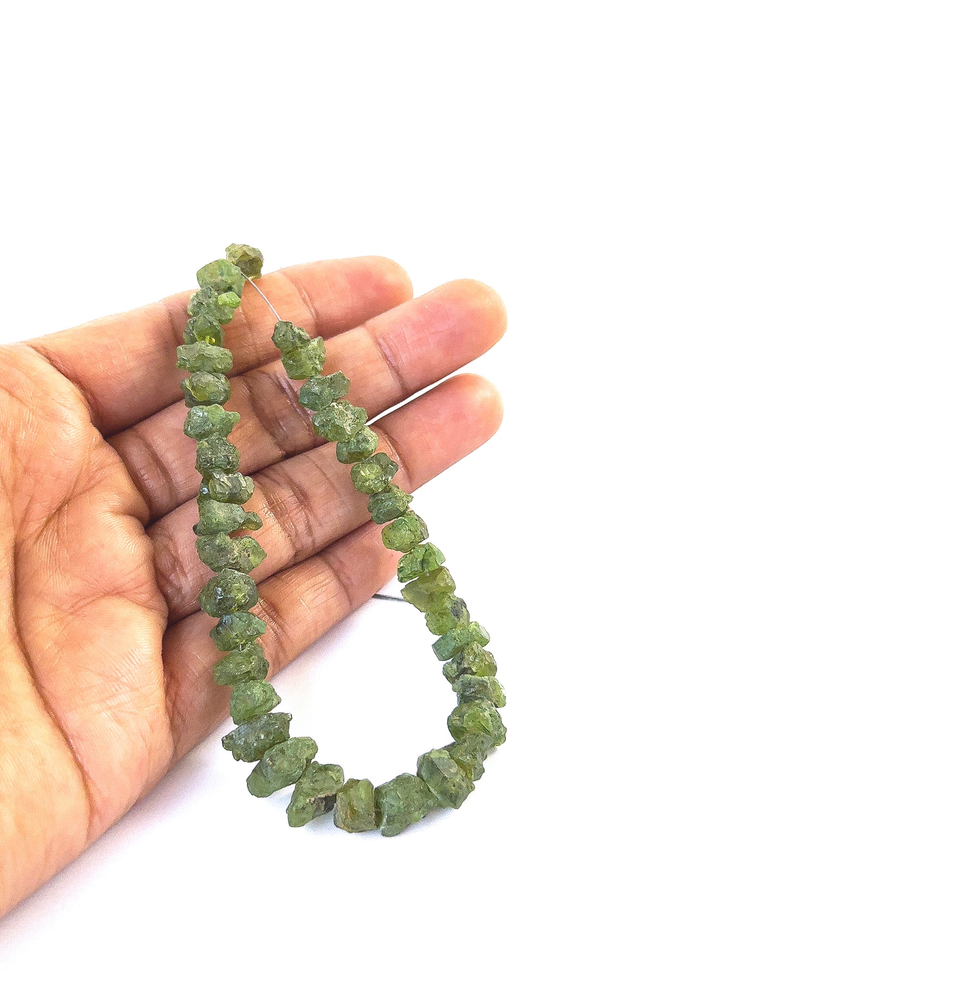 A person holds delicate pieces of Peridot drilled rough beads, showcasing their natural raw texture.