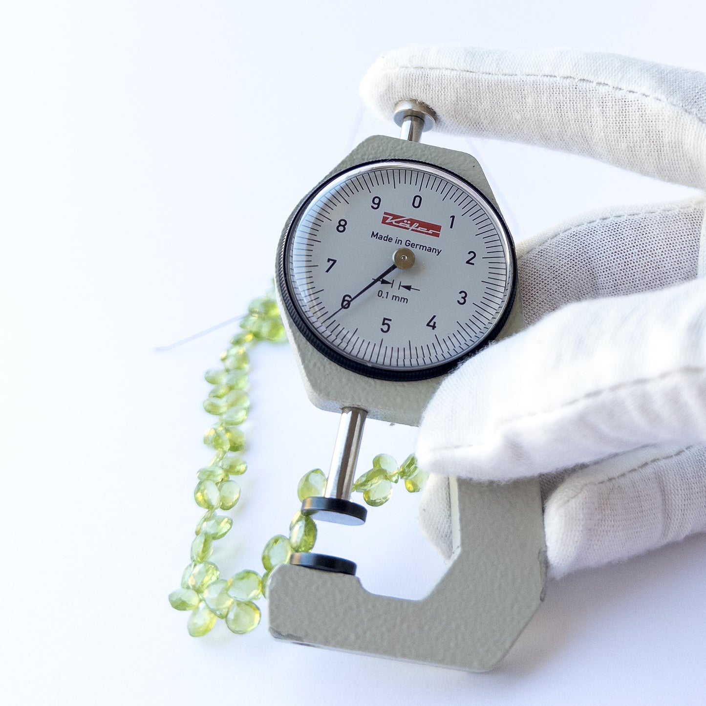 A dial gauge measures the Peridot faceted briolette 5.5–6mm gemstone.