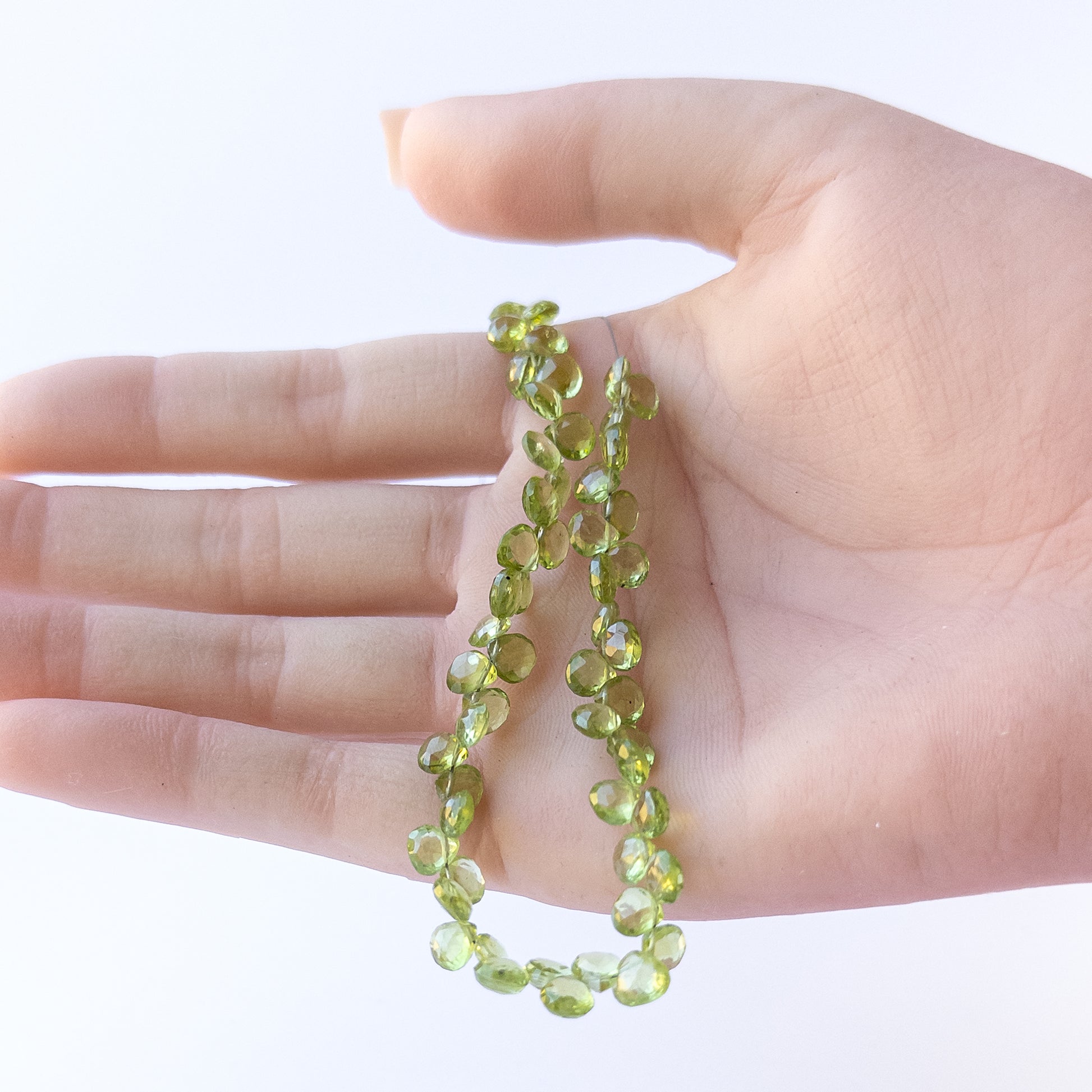 A person holds delicate strands of Peridot beads, showcasing their faceted briolette design.