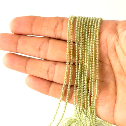 A person holds delicate strands of Peridot beads, showcasing their faceted rondelle design.