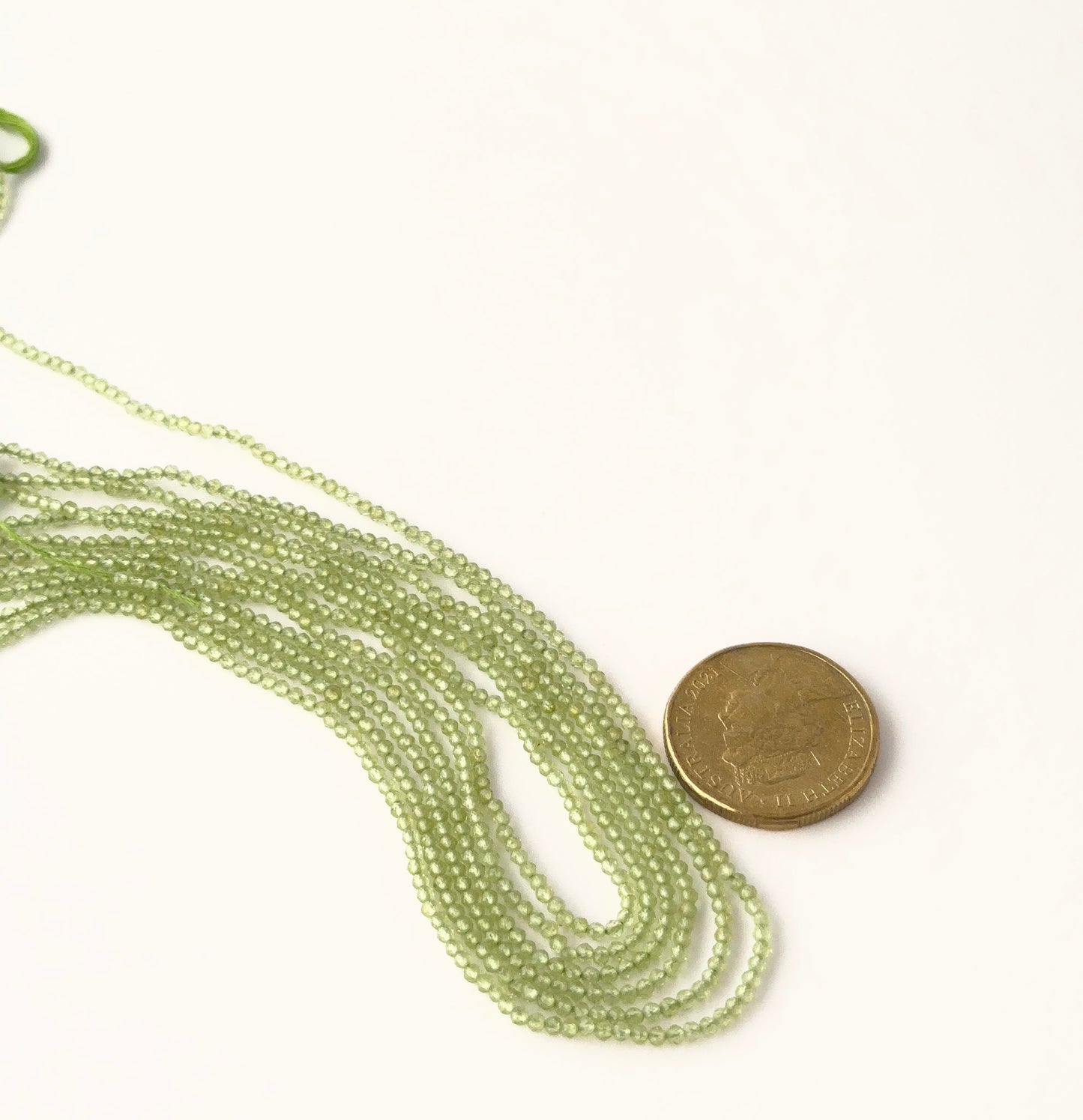 A coin is placed near delicate strands of Peridot beads for scale