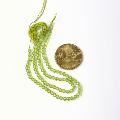 A coin is place near delicate strands of Peridot beads for scale.