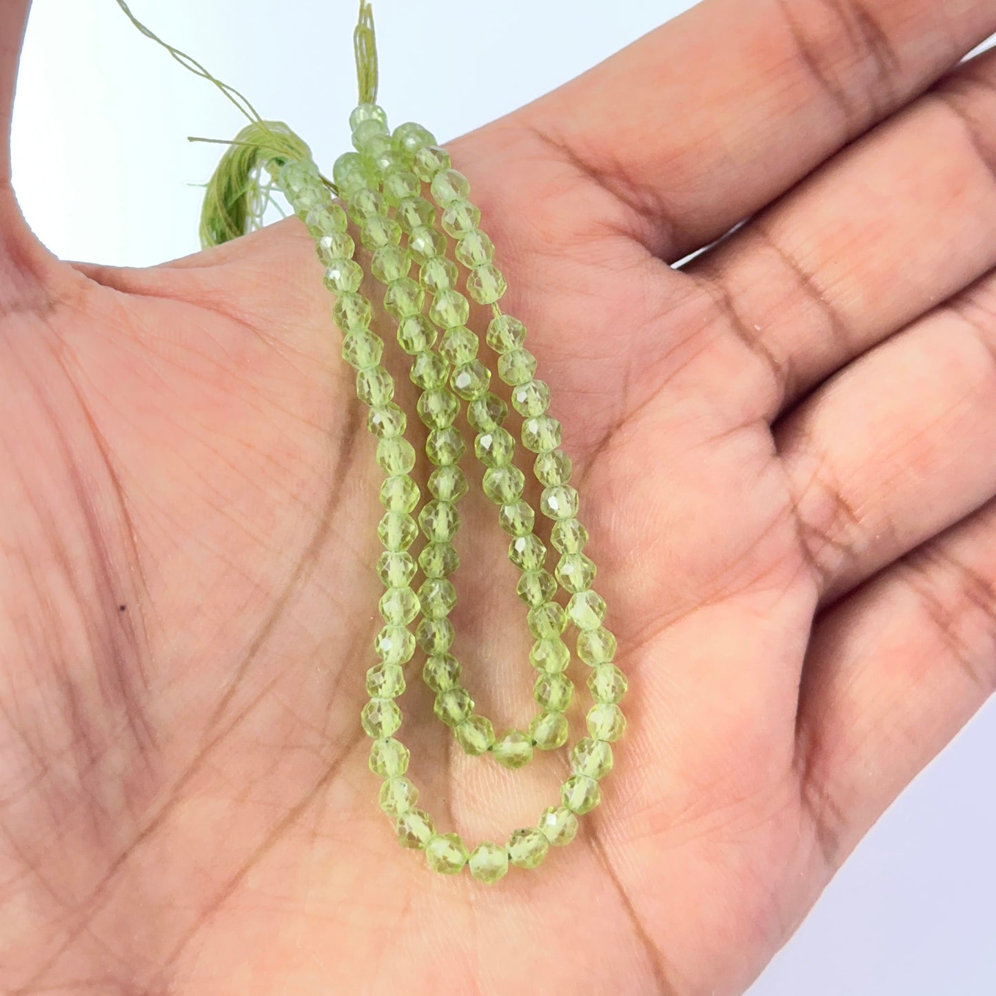 A person holds delicate strands of Peridot beads, showcasing their faceted rondelle design.