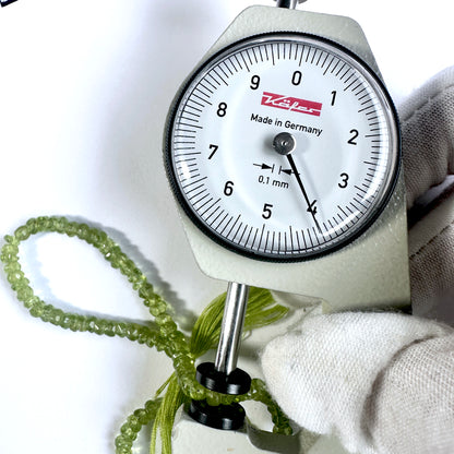 A dial gauge measures the Peridot faceted rondelle 4mm gemstone.