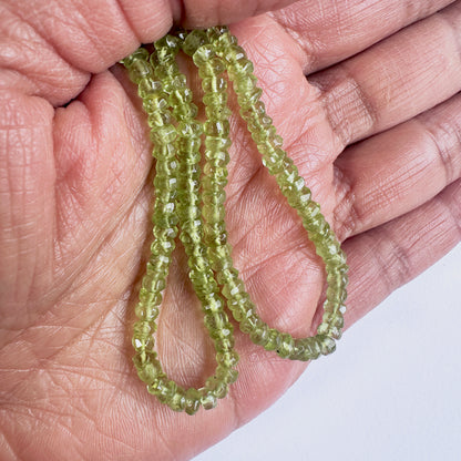 A person holds delicate strands of Peridot beads, showcasing their smooth design.