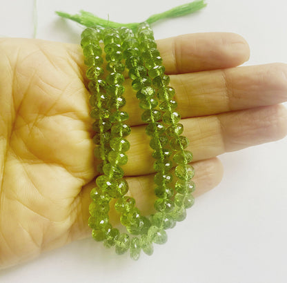 A person holds delicate strands of Peridot beads, showcasing their smooth design. 