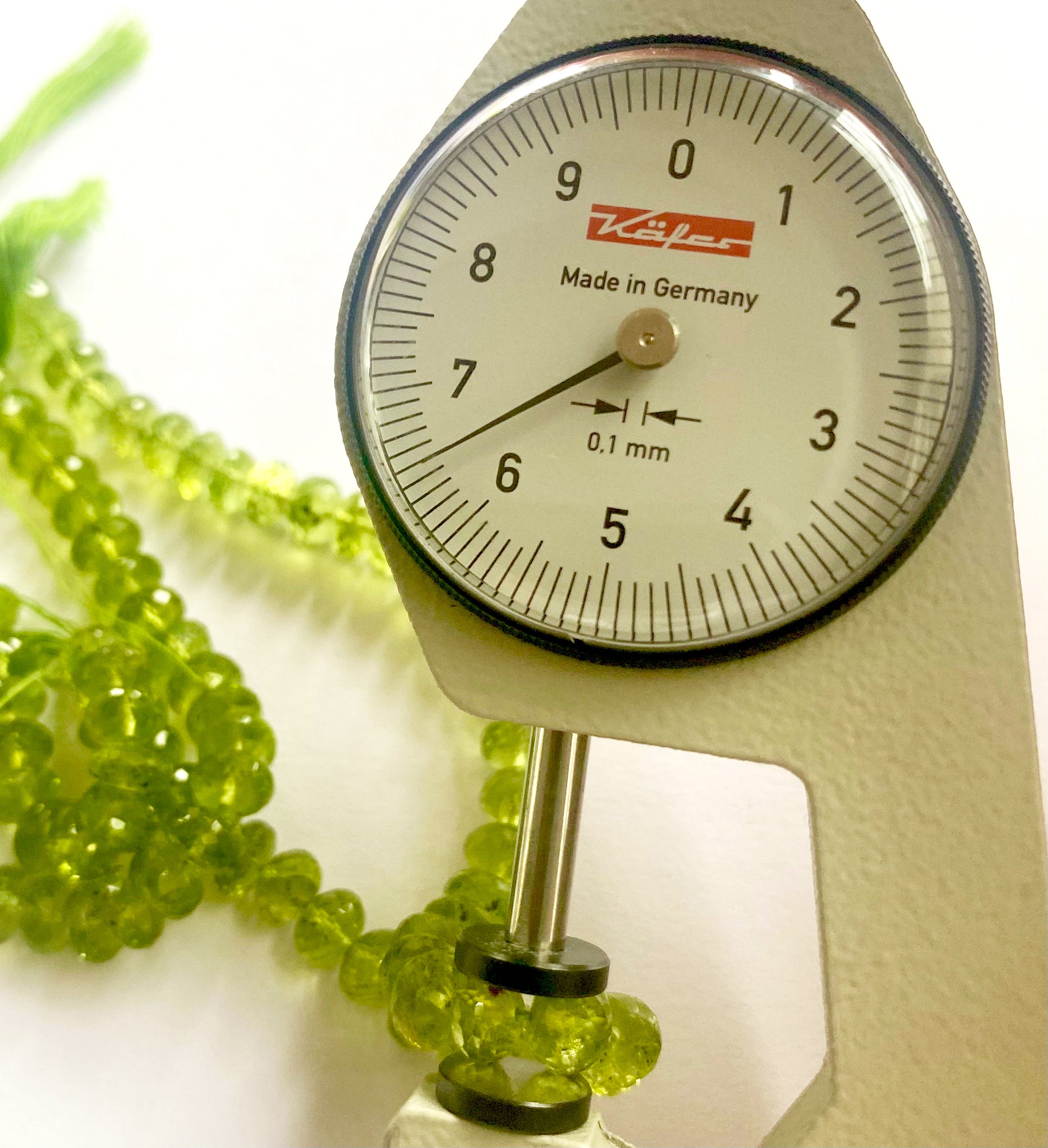 Dial gauge measuring a faceted rondelle Peridot gemstone bead sized 6.5–6.7mm. 