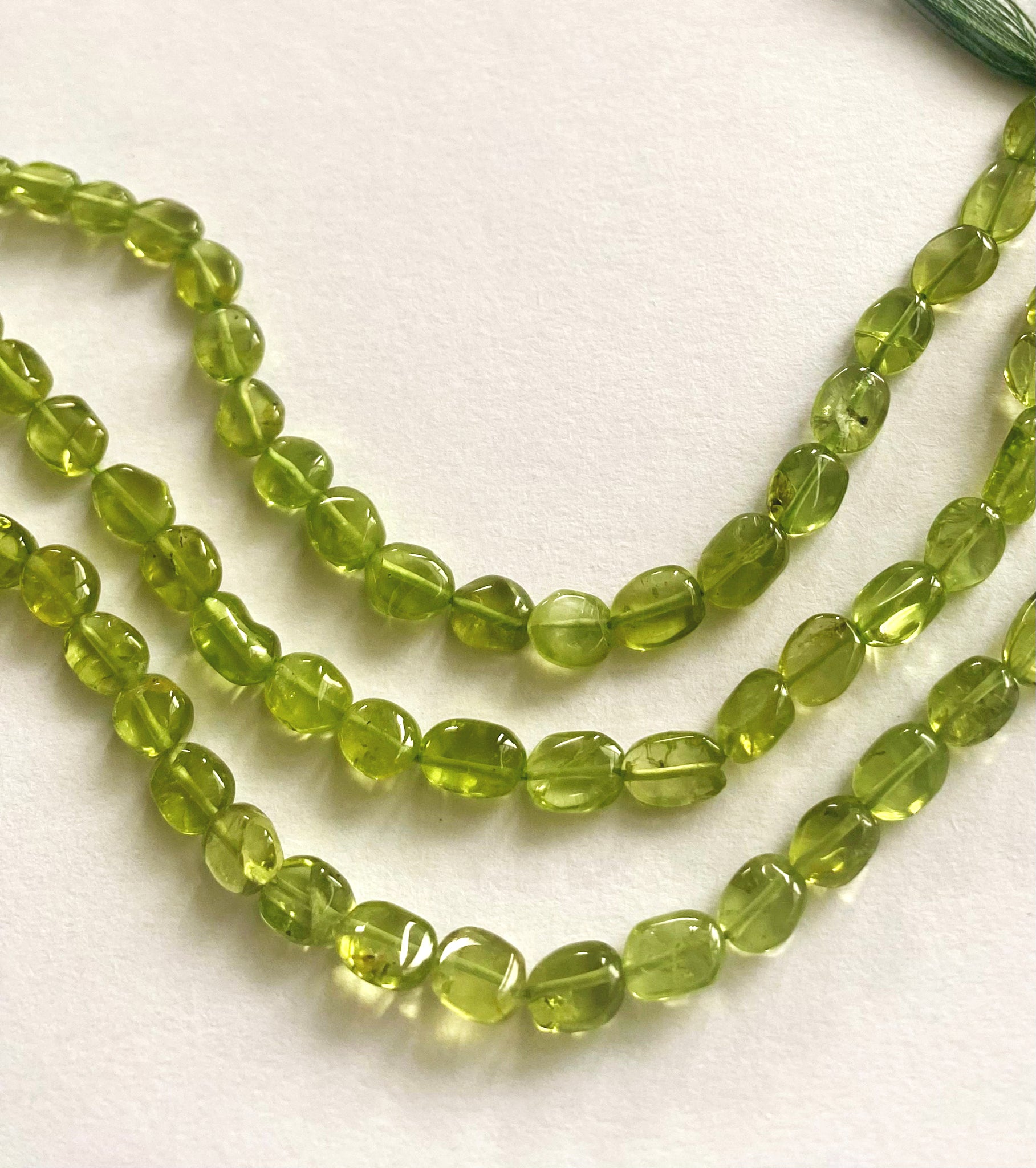 Strand of peridot beads with 6.5–7.5mm size, highlighting their smooth finish and bright colour.