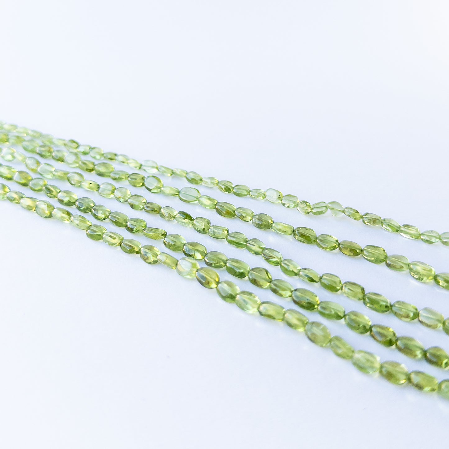 Peridot smooth oval beads displaying soft translucency and vibrant green tones.