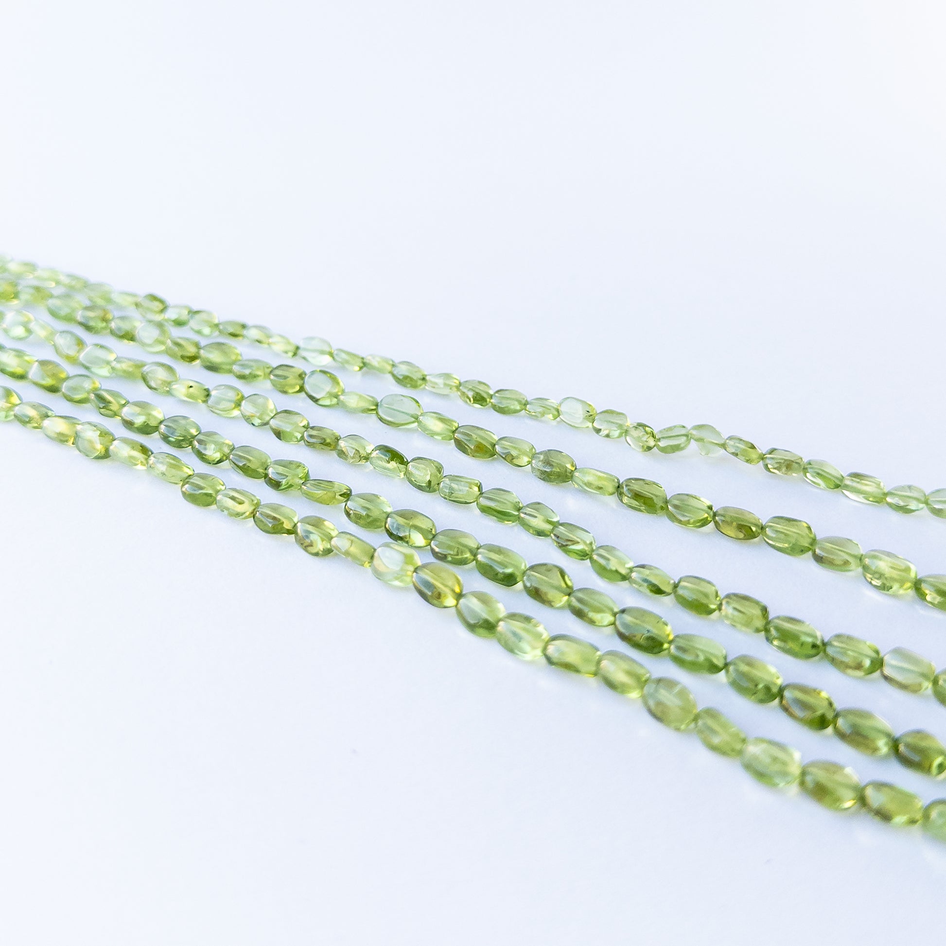 Peridot smooth oval beads displaying soft translucency and vibrant green tones.