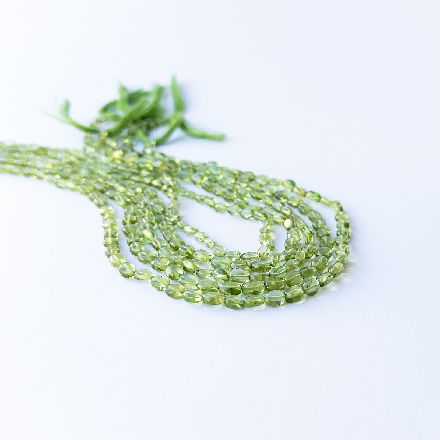 Peridot smooth oval gemstone beads arranged in a strand for handmade jewellery making.