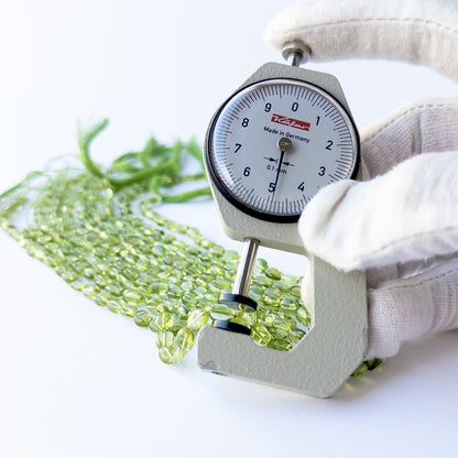 A dial gauge measures the Peridot smooth oval 4–5mm gemstone.