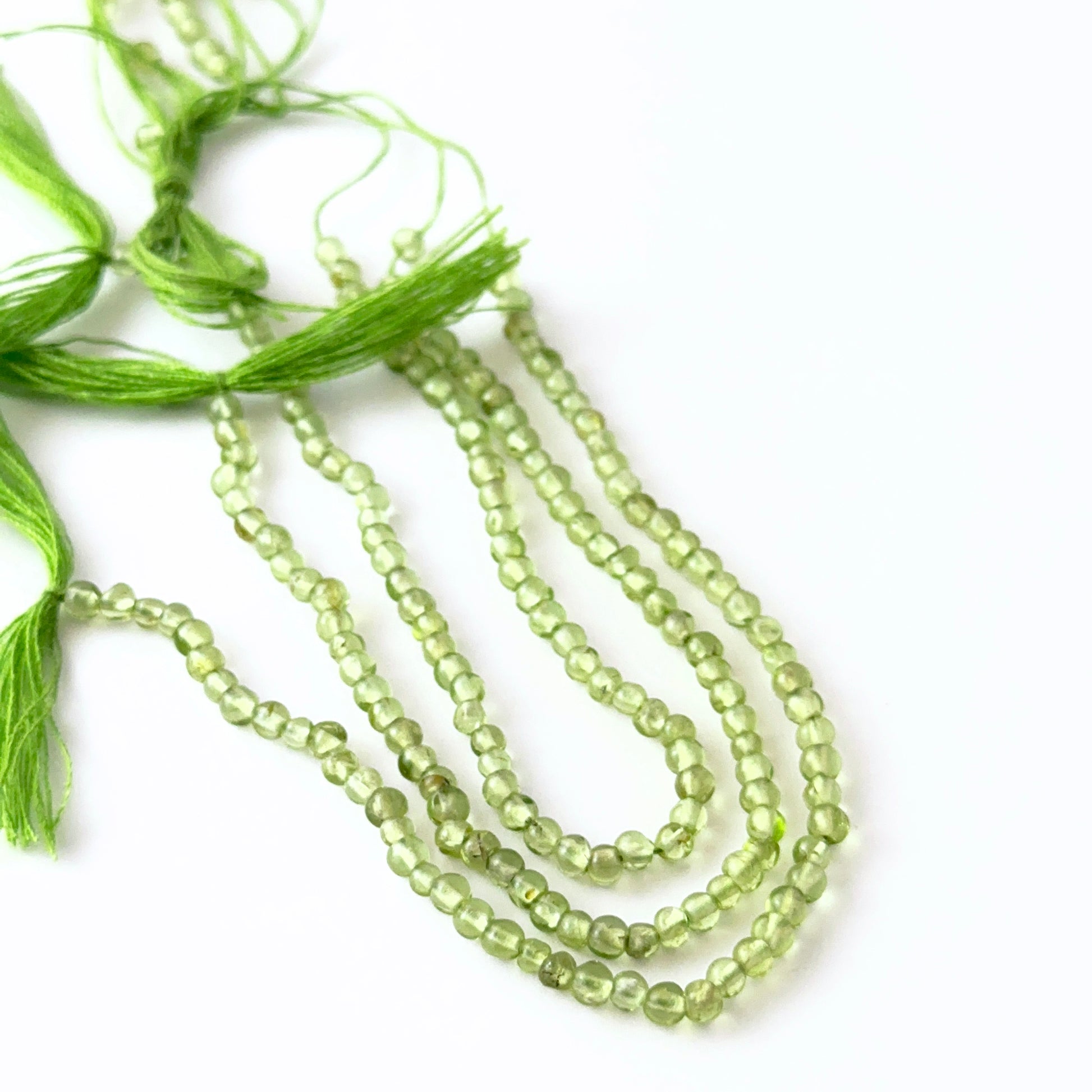 Peridot smooth round beads in multiple strand lengths, displaying vibrant green tones and elegant handcrafted appeal.