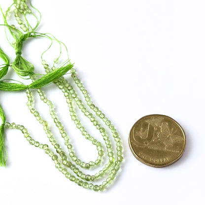 A coin is placed near delicate strands of Peridot beads for scale.