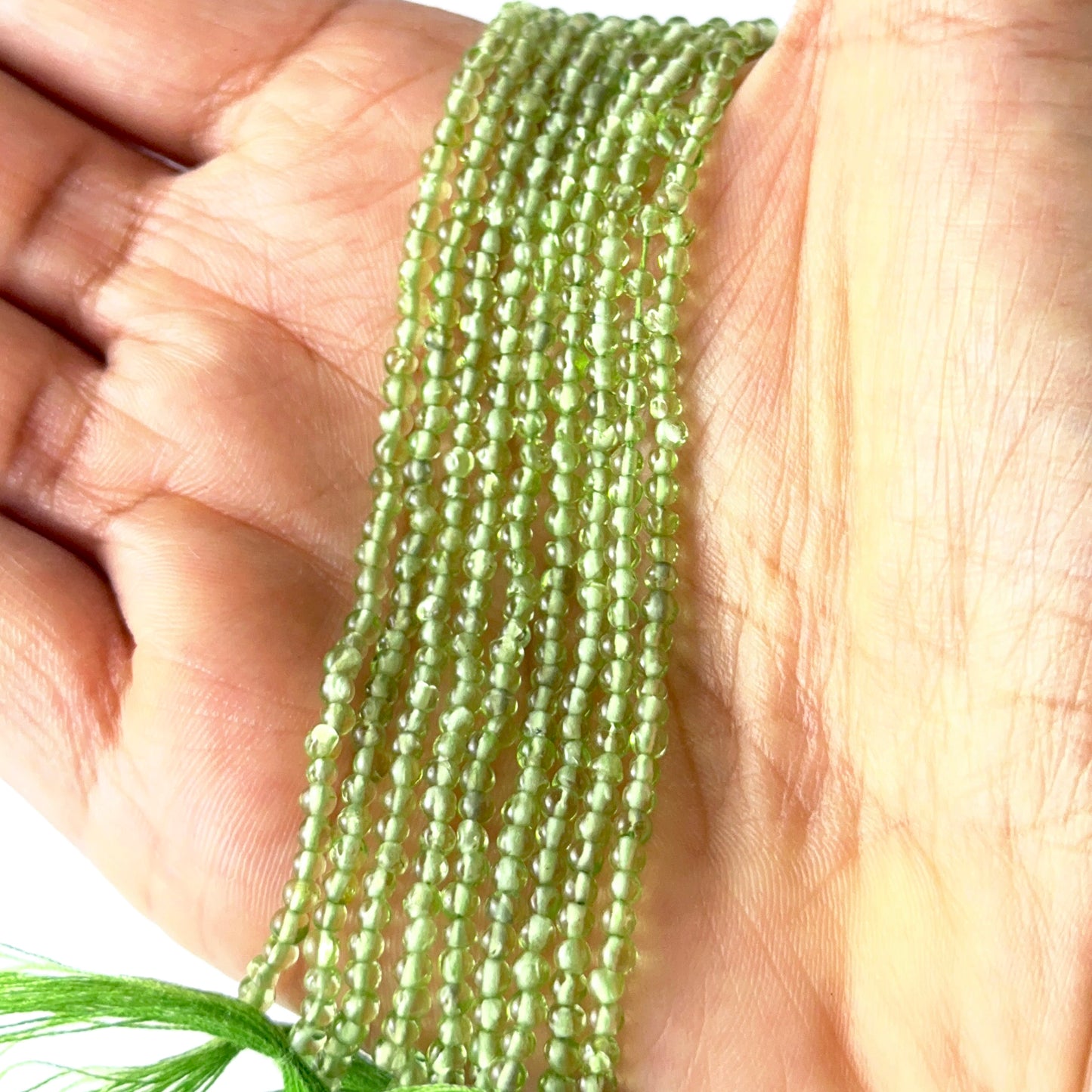 A person holds delicate strands of Peridot beads, showcasing their smooth round design