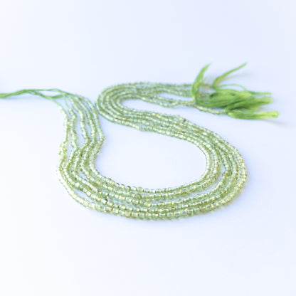 Peridot smooth round beads in 2.7–3mm size arranged in a strand, showing bright green tones for handmade jewellery components.