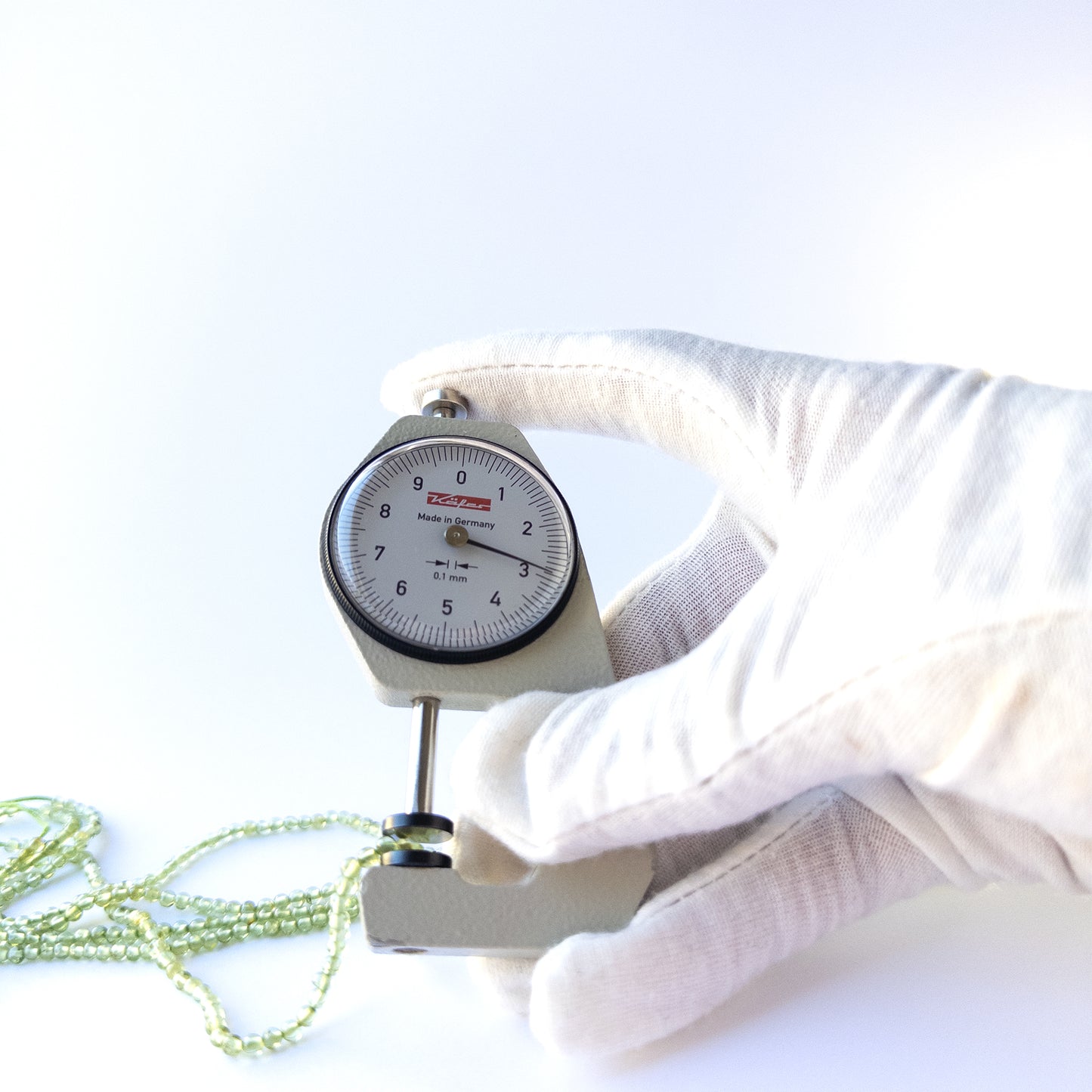 A dial gauge measures the Peridot Smooth Round 2.7–3mm gemstone.