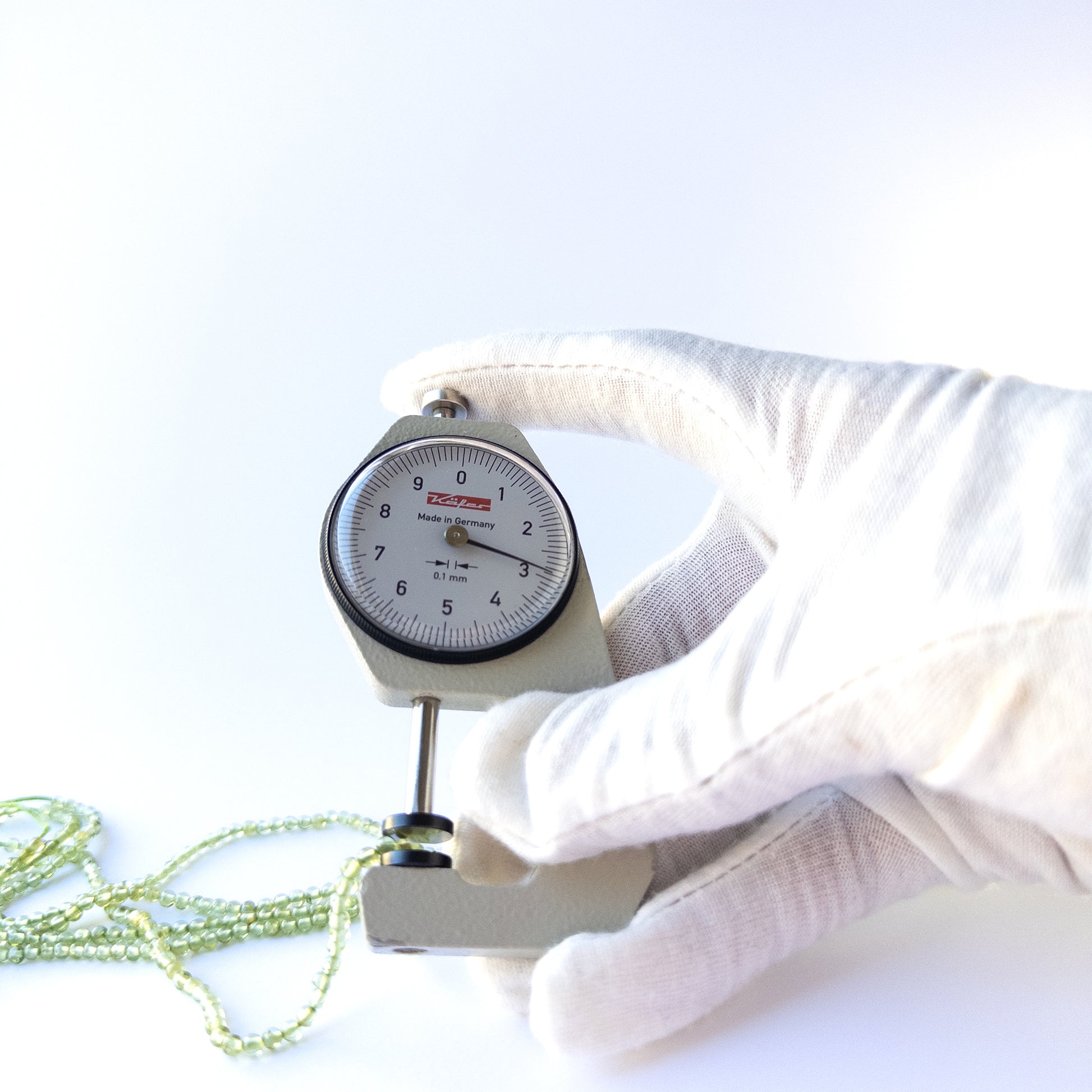 A dial gauge measures the Peridot Smooth Round 2.7–3mm gemstone.