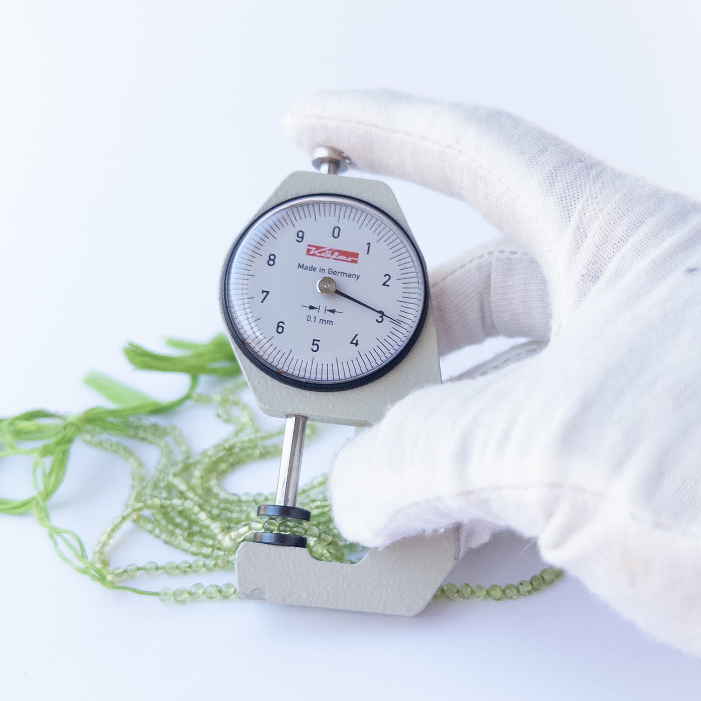 A dial gauge measures the Peridot smooth round 2.8mm bead size gemstone.
