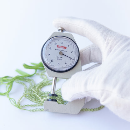 A dial gauge measures the Peridot smooth round 2.8mm bead size gemstone.