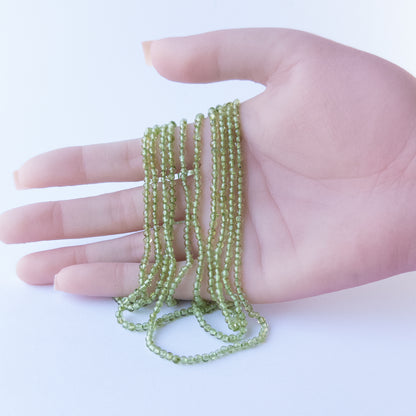 A person holds delicate strands of Peridot beads, showcasing their smooth round design.