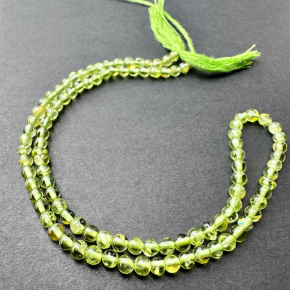 Peridot smooth round beads with bright green tones arranged on a 33cm strand for jewellery making.