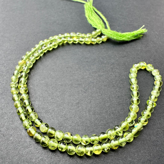 Peridot smooth round beads with bright green tones arranged on a 33cm strand for jewellery making.