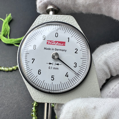 A dial gauge measures the Peridot smooth round 3.5mm gemstone.