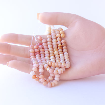A person holds delicate strands of Peruvian Opal beads, showcasing their faceted rondelle design.